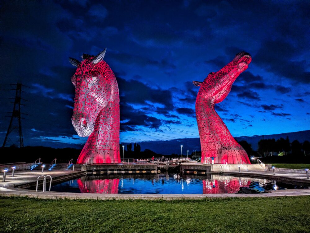 Two horse head sculptures lit up in red at night